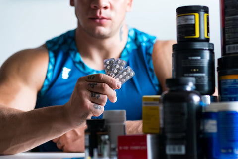 Bodybuilder sat with a selection of vitamins to assist with diet and training